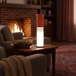 May include: A modern, cylindrical table lamp with a red top, white center, and black base. The lamp is on a dark wood side table next to a stack of books. The background includes a fireplace and a cozy living room setting.