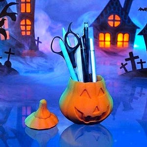 May include: An orange pumpkin-shaped container with a carved jack-o'-lantern face, holding black scissors, a white marker, and two pens. A separate orange pumpkin lid sits to the left of the container, all set against a blue-lit spooky background.