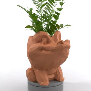 May include: A brown, geometric-shaped planter in the form of a crocodile, holding green leafy plants. The planter sits on a gray base. The crocodile planter is a unique decorative item for home or office.