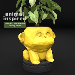 Puede incluir: Una maceta amarilla con forma de perro geométrico con una planta dentro. La maceta se asienta sobre una base gris oscuro. Las palabras "animal inspired" están encima de la maceta, con "planter, pen holder, candy bowl" debajo.