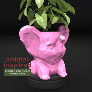 May include: A pink, geometric elephant-shaped planter holding a green leafy plant. The planter sits on a dark gray base. Text on the image reads "animal inspired" and "planter, pen holder, candy bowl."