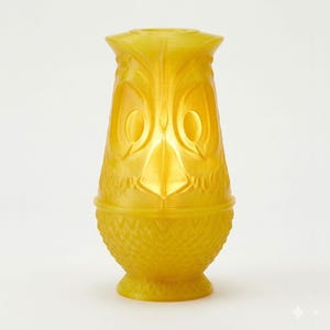 May include: A yellow owl-shaped vase. The vase has a textured surface and features large, oval-shaped eyes and a beak. The base of the vase has a textured, scale-like pattern. The vase is approximately 15 cm tall.