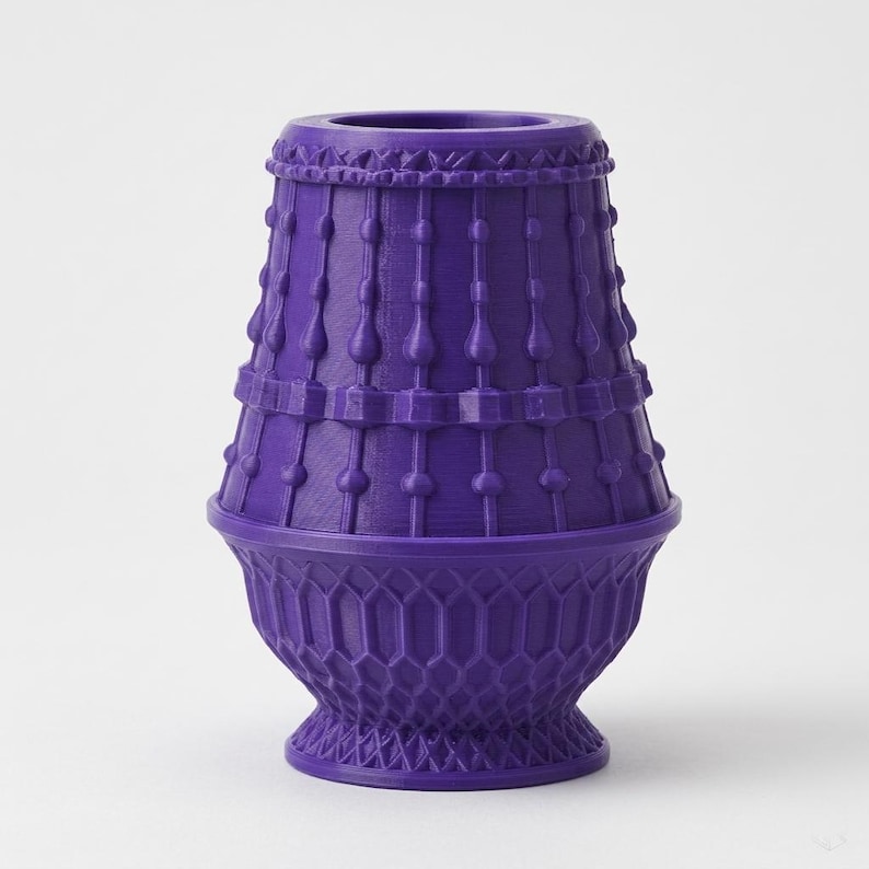 May include: A vibrant purple vase featuring a tapered cylindrical top section adorned with vertical beaded columns and a wider, rounded base section decorated with a textured, repeating honeycomb lattice pattern throughout the lower exterior.