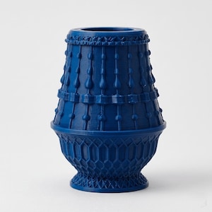 May include: A deep blue vase with a textured surface featuring a geometric lattice pattern at the base and vertical, spindle-like decorative elements extending upward toward the rim, creating a structured and symmetrical appearance.