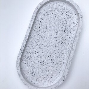 May include: A white oval tray with a speckled finish. The tray is made of concrete and has a raised rim.