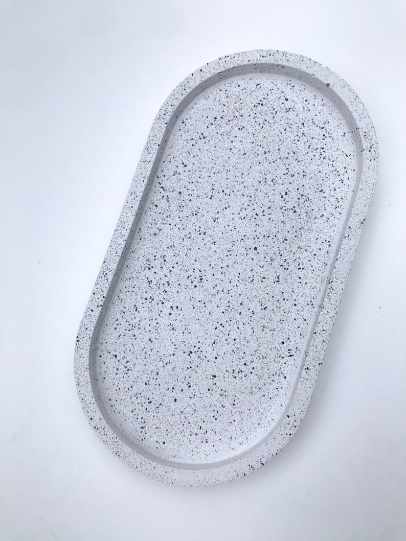 May include: A white oval tray with a speckled finish. The tray is made of concrete and has a raised rim.