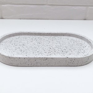 May include: White oval tray with a speckled finish. The tray is made of concrete and has a slightly raised rim.