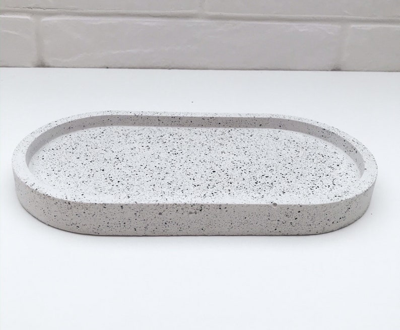 May include: White oval tray with a speckled finish. The tray is made of concrete and has a slightly raised rim.