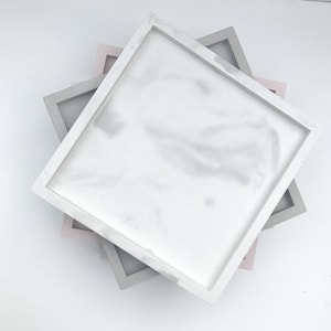 May include: Three square trays stacked on top of each other. The top tray is white with a marble pattern, the middle tray is grey, and the bottom tray is pink.