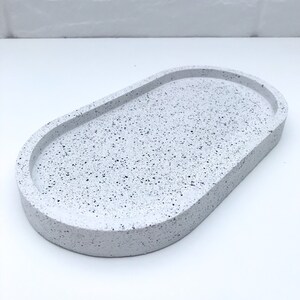 May include: White oval tray with a speckled finish. The tray is made of concrete and has a smooth, rounded edge.