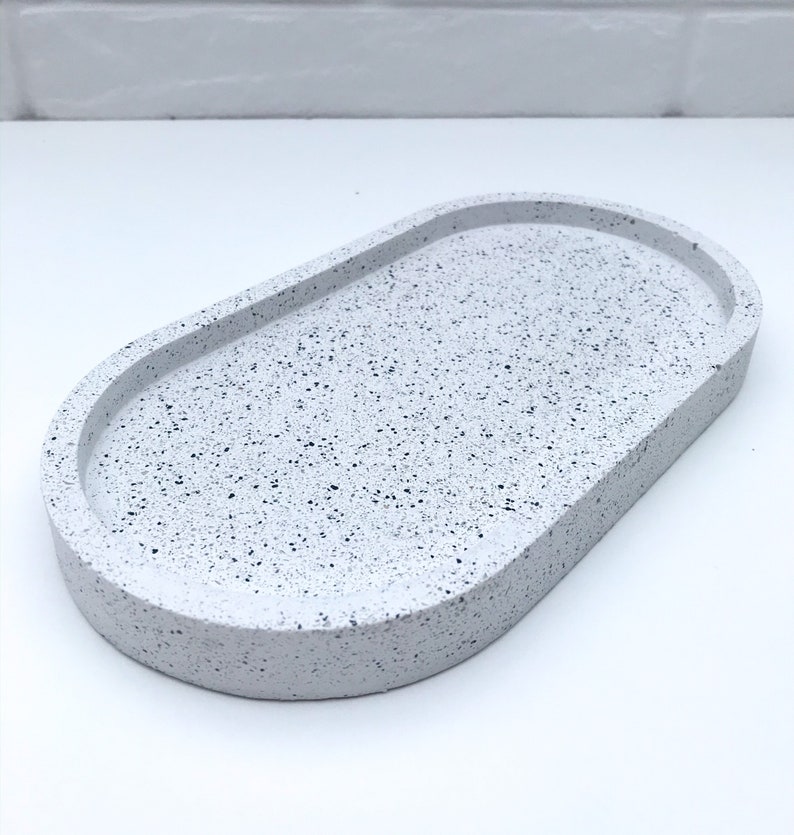 May include: White oval tray with a speckled finish. The tray is made of concrete and has a smooth, rounded edge.