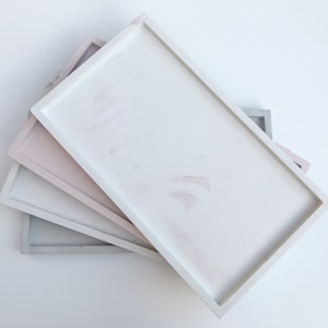 May include: Three rectangular trays stacked on top of each other. The top tray is white, the middle tray is light pink, and the bottom tray is light grey.