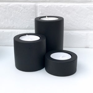 May include: Three black concrete candle holders of varying sizes. The candle holders are round and have a smooth, matte finish.