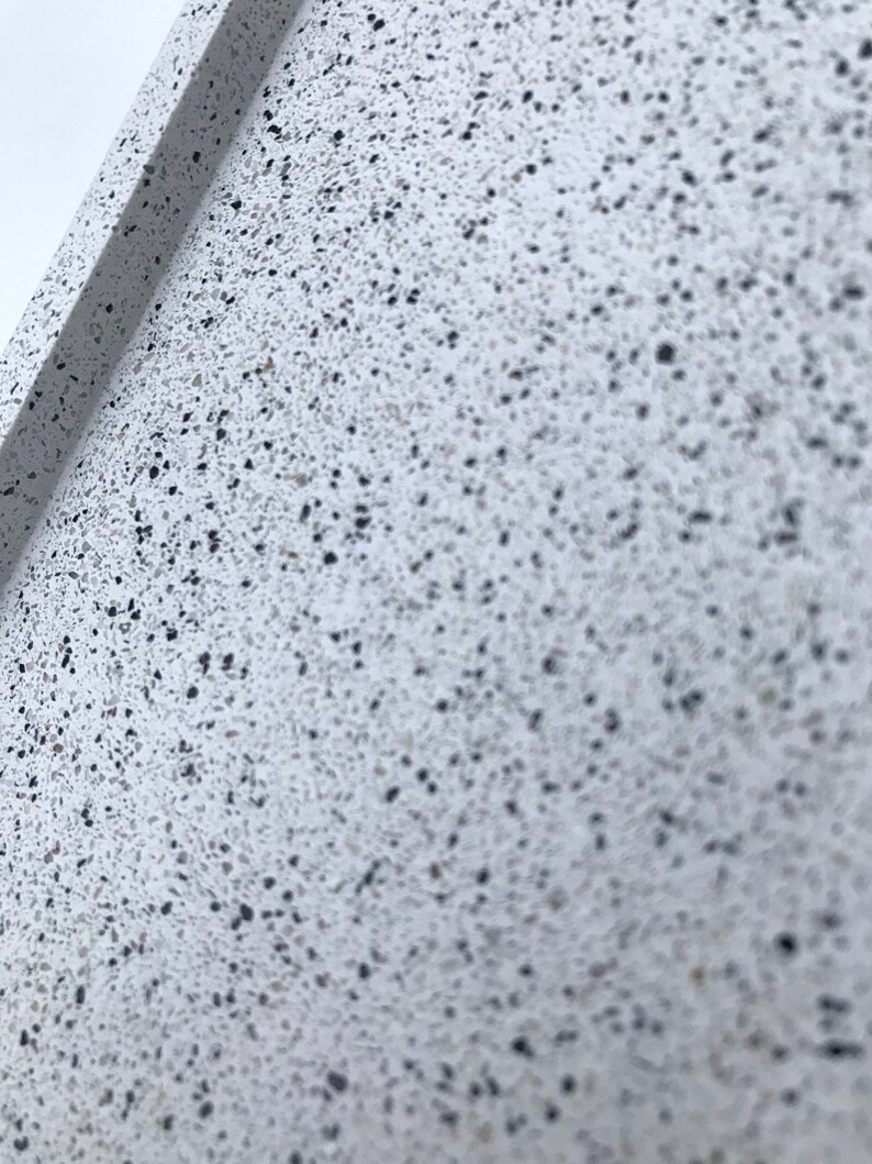 May include: Close-up of a white surface with small black flecks. The surface has a rough texture.