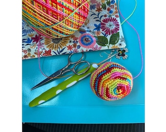 May include: Image of a crochet pattern with the text "HAPPY SACK CROCHET PATTERN" by RusticPixels. The image shows a ball of colorful yarn, a crochet hook, scissors, and a finished crocheted ball on a blue surface.