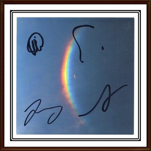 May include: A framed print featuring a vibrant rainbow arcing across a blue sky. The rainbow displays a full spectrum of colors. The image is signed in black ink with four distinct signatures. The frame is a dark brown color.
