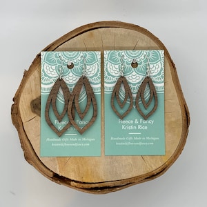 May include: Two pairs of brown wooden earrings with a double leaf design. The earrings are displayed on a card with the text "Fleece & Fancy Kristin Rice" and "Handmade Gifts Made in Michigan kristin@fleeceandfancy.com".