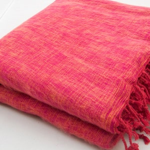 以下が含まれることがあります： フリンジの付いたピンクとオレンジの織り毛布