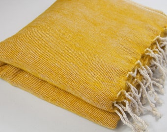 Pode incluir: Uma manta amarela dobrada com franjas brancas. A manta é feita de um tecido macio e texturizado.