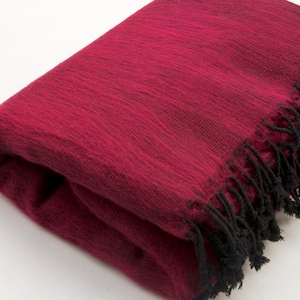 Peut inclure: Couverture bordeaux pliée avec des franges noires. La couverture a un aspect doux et texturé. La frange est de couleur noire unie et se trouve sur un bord de la couverture. La couverture est pliée sur elle-même.