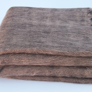 May include: Folded brown blanket with a textured weave and dark fringe. The blanket is made of a soft material and is folded into three layers, showcasing its thickness and warmth. The colour is a mix of brown and tan.