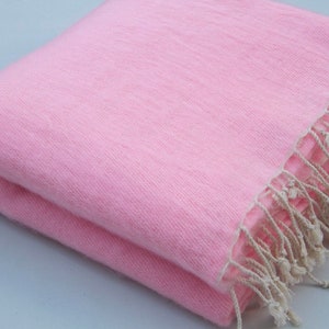 May include: A soft pink throw blanket with a fringe border. The blanket is folded in half and the fringe is visible on the right side of the image.