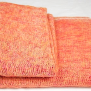 May include: A folded orange and pink woven shawl with a fringe border.