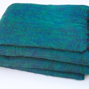 Peut inclure: Plaid tissé vert et bleu plié avec des franges noires. La couverture est faite d'un matériau doux et texturé et est pliée proprement. La frange est le long d'un bord de la couverture.