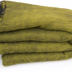 Pode incluir: Cobertor verde-oliva dobrado com franjas pretas. O cobertor &eacute; feito de um tecido texturizado e est&aacute; cuidadosamente empilhado. A franja escura adiciona um detalhe contrastante &agrave; borda do cobertor. Um t&ecirc;xtil dom&eacute;stico aconchegante.