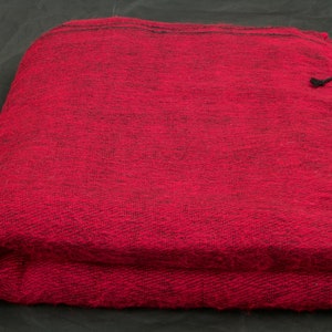 May include: A folded red blanket with black fringe. The blanket is a solid, deep red color with a woven texture. The fringe is a contrasting black color. The blanket appears soft and warm.