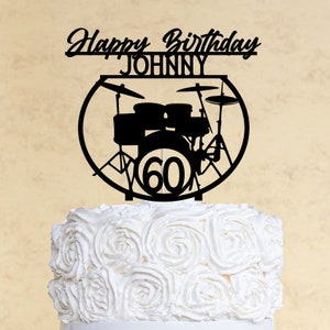 May include: Black and white silhouette of a drum set with the number 60 in the center. The text "Happy Birthday JOHNNY" is above the drum set. The drum set is on top of a white cake with white frosting.
