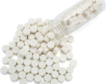 May include: A glass jar filled with white wax sealing beads, spilling out onto a white surface. The beads are hexagonal in shape.
