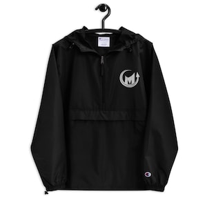 May include: Black Champion brand windbreaker jacket with a zipper closure and a silver embroidered logo on the front. The logo is a circle with an arrow pointing upwards and the letter "M" inside the circle.
