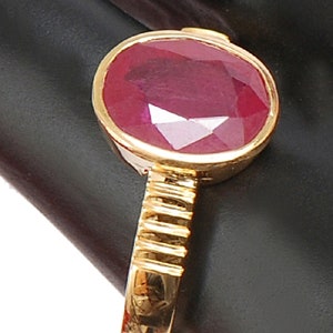 May include: A gold ring with a large, oval-shaped ruby gemstone. The ruby is a deep red color and has a faceted cut.