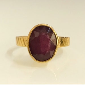 May include: A gold ring with a deep red oval gemstone. The ring band has a textured design.
