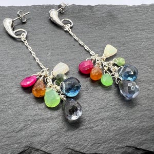 May include: A pair of silver dangle earrings featuring a cluster of colourful gemstones, including pink, red, green, blue, and orange.