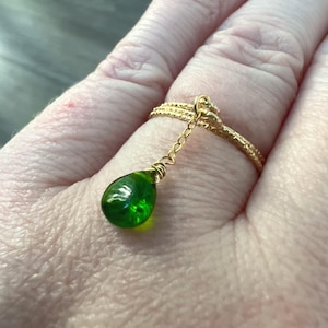 May include: A gold ring with a delicate chain and a dangling green teardrop-shaped gemstone.