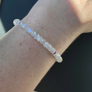 May include: A white gemstone bracelet with small red beads interspersed throughout.