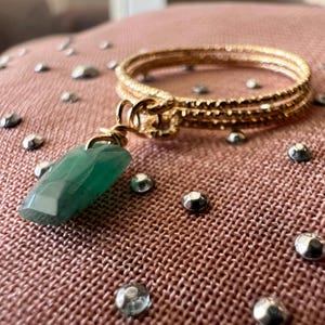 May include: A gold bangle bracelet with a green gemstone pendant. The bracelet is made of three thin bands of gold metal.