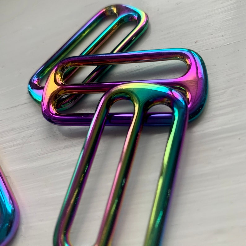 May include: Three iridescent metal slider buckles in a rainbow finish. The buckles are stacked on top of each other.