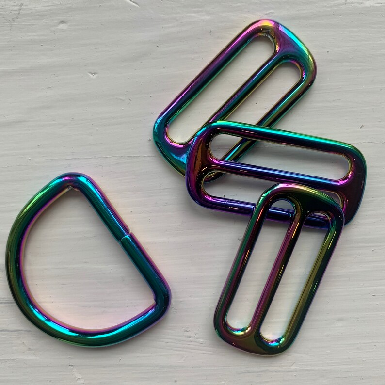 May include: Four iridescent metal D-rings in various sizes. The rings are a rainbow of colors, including purple, blue, green, and red.