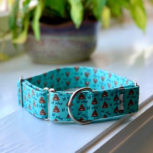 Puede incluir: Un collar para perro azul turquesa con una hebilla plateada. El collar está cubierto de un patrón repetido de emojis de caca marrones y el texto "lil shit".