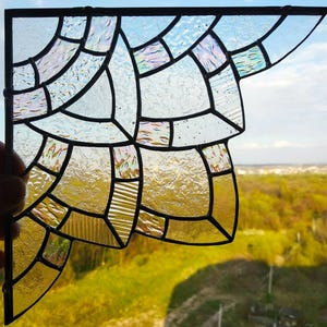 Op de afbeelding: Een hoekvormig glas-in-loodpaneel met een geometrisch raster van getextureerde glasstukken. Het ontwerp verloopt van helder, iriserend glas aan de bovenkant naar warm geel glas aan de onderkant, alles samengevoegd door donkere metalen soldeerlijnen.