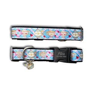 May include: A dog collar featuring a blue and pink plaid design with teacups, teapots, and hearts. The collar has a black buckle with the name "Alice" and a phone number. A small charm hangs from the collar.
