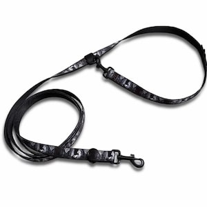 May include: Black dog leash with a repeating pattern of white ghost-like figures. The leash has a black metal clasp and a loop handle. The leash is designed for walking dogs and other pets.