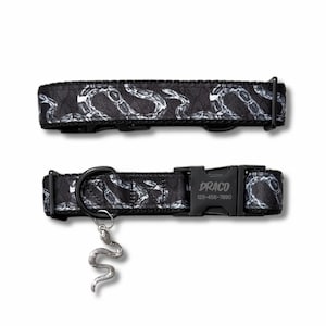May include: A black pet collar featuring a white snake pattern, a black plastic buckle engraved with the text DRACO and 123-456-7890, a black metal D-ring, and a silver-toned snake-shaped charm hanging from the ring, shown in two views.