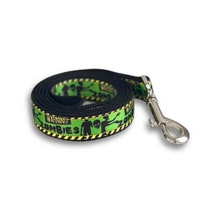 May include: Black dog leash with a green and yellow zombie-themed pattern. The pattern includes zombie silhouettes and the words "WARNING ZOMBIES". The leash has a silver metal clasp.