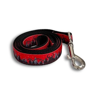 Puede incluir: Una correa para perros negra y roja enrollada con un cierre de metal plateado. La parte roja presenta una escena de bosque con siluetas de árboles y una criatura con cuernos. Diseñado para dueños de mascotas.