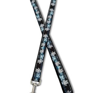 May include: A fabric lanyard featuring a repeating pattern of small, light-colored cartoon goat heads against a dark blue and black forest background. The strap is finished with a silver-toned metal swivel lobster claw clasp at the bottom end.