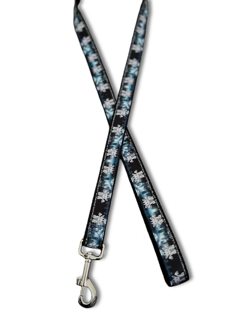 May include: A fabric lanyard featuring a repeating pattern of small, light-colored cartoon goat heads against a dark blue and black forest background. The strap is finished with a silver-toned metal swivel lobster claw clasp at the bottom end.